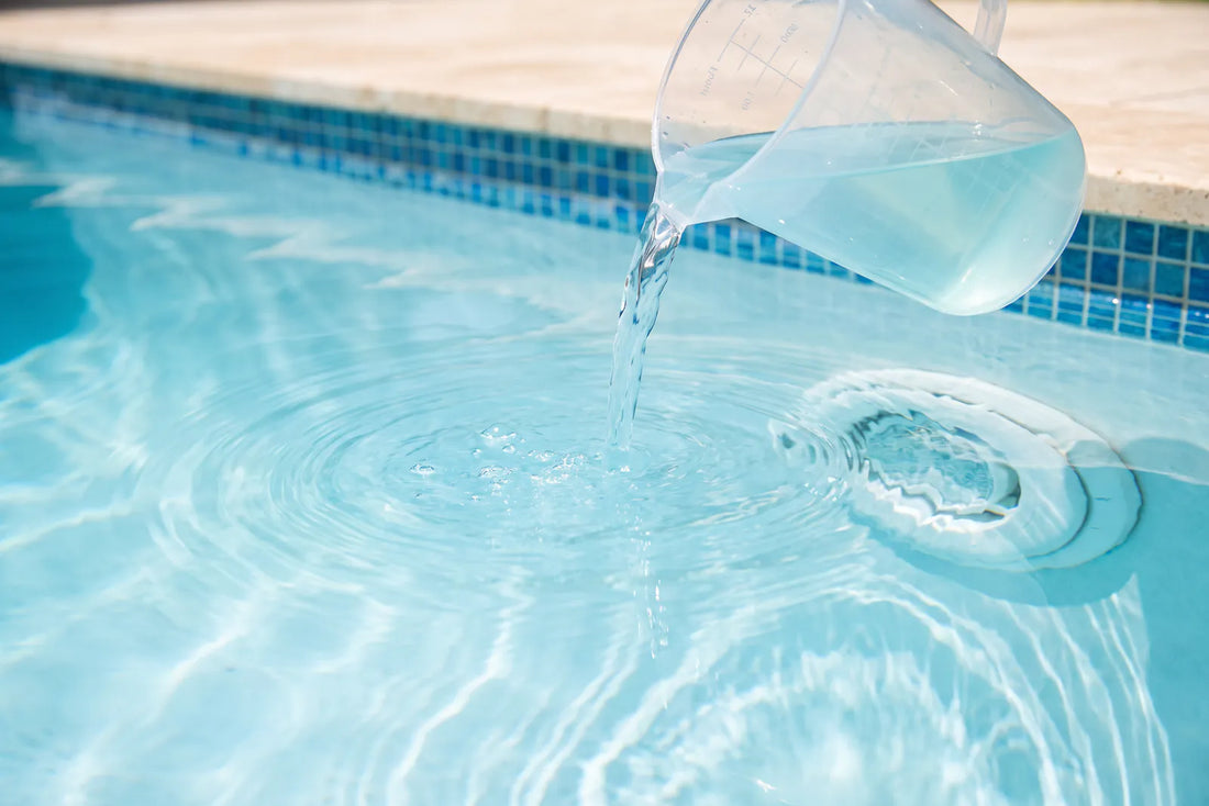Alguicida líquido siendo dosificado en el borde de una piscina de agua clara